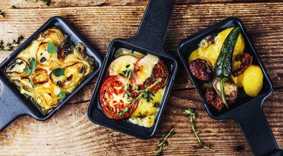 Raclette-Pfännchen von oben fotografiert auf einer Holzplatte