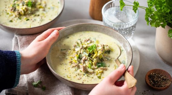 Zwei Hände halten einen Teller mit heller Suppe, garniert mit Kräutern – Foto: Anna Gieseler