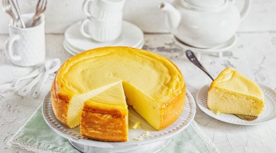 Ein Teller mit Käsekuchen, von dem schon zwei Stücken abgeschnitten sind. Im Hintergrund helles Geschirr