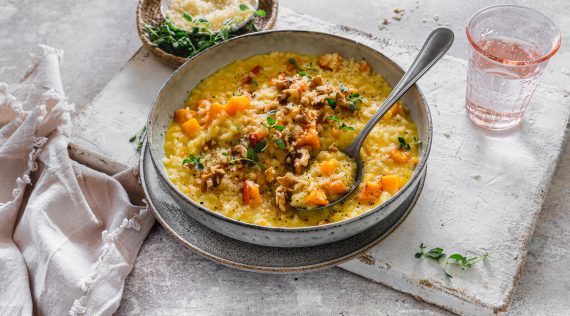 Kürbisrisotto auf einem grauen Teller, mit gehackten Nüssen garniert – Foto: Tina Bumann