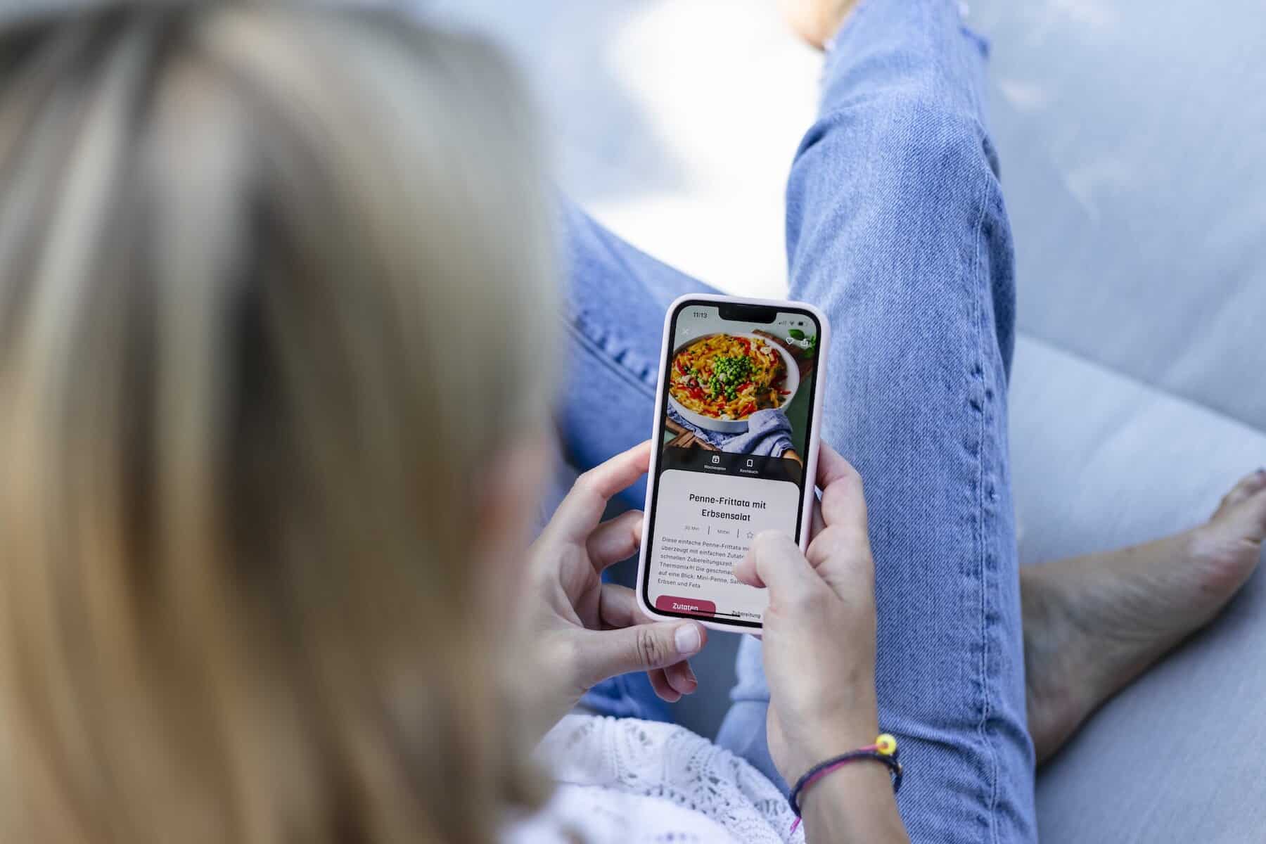 Eine Frau hält ein Handy, auf dem ein Rezept angezeigt wird. Wir blicke über ihre Schulter auf das Smartphone