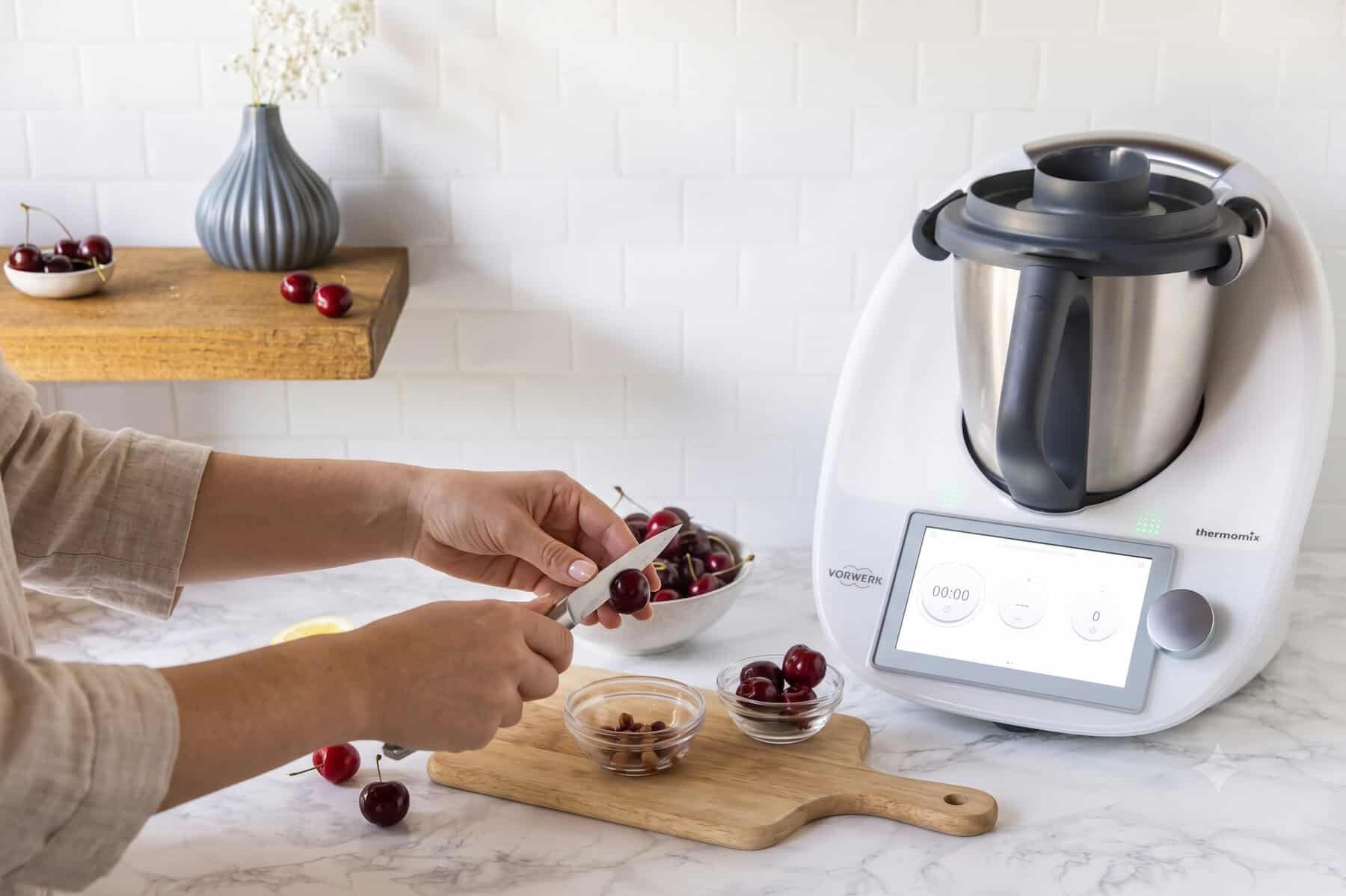 Zwei Hände halten eine Kirsche und ein Messer und im Hintergrund steht ein Thermomix®