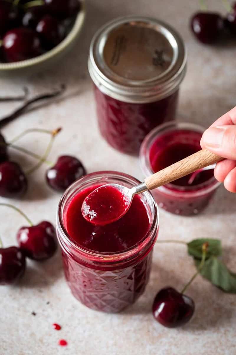 Drei Gläser Kirschmarmelade jemand entnimmt etwas mit einem Löffel
