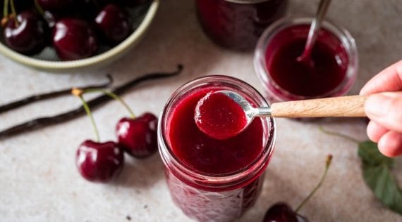 Drei Gläser Kirschmarmelade jemand entnimmt etwas mit einem Löffel
