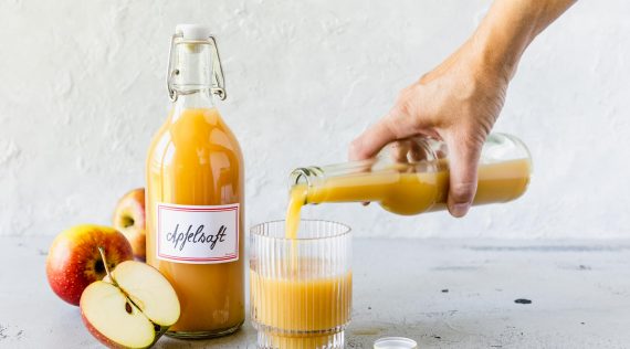 Eine Flasche mit Apfelsaft und ein Glas, in das jemand Saft gießt