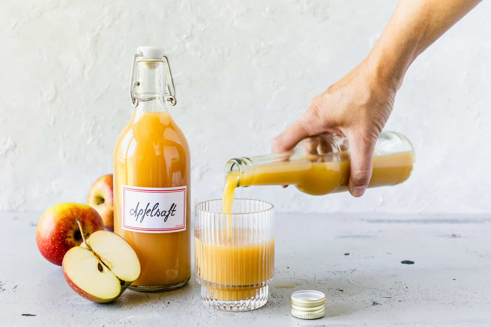 Eine Flasche mit Apfelsaft und ein Glas, in das jemand Saft gießt