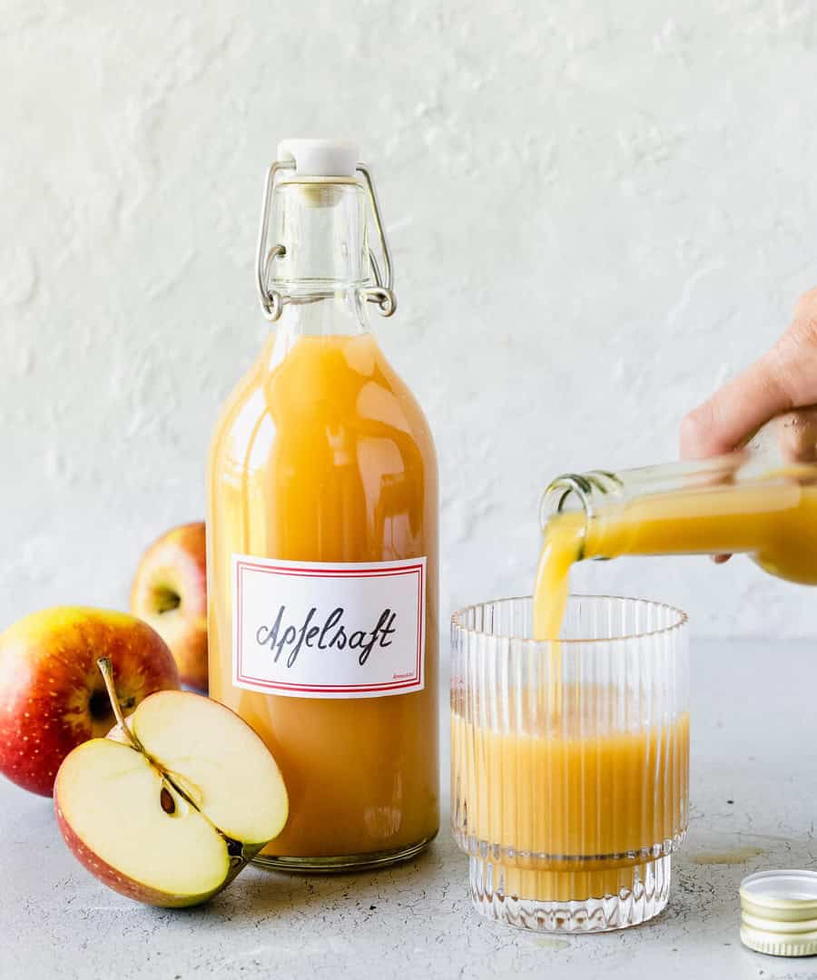 Eine Flasche mit Apfelsaft und ein Glas, in das jemand Saft gießt