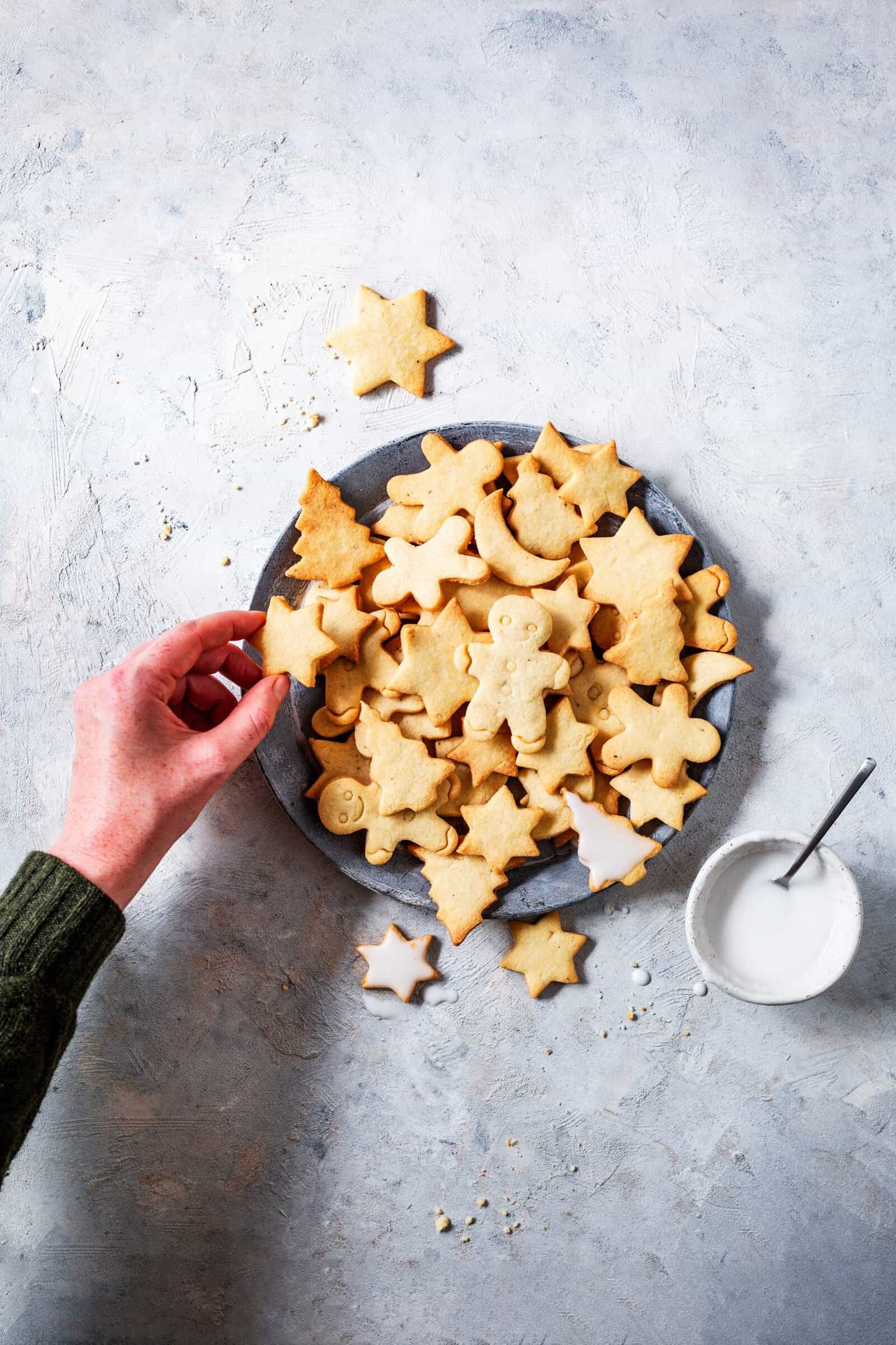 Ein Teller mit Plätzchen von oben fotografiert. Eine Hand nimmt ein Plätzchen – Foto: Anna Gieseler
