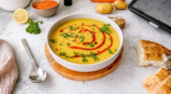 Ein Teller mit orangefarbener Suppe mit rotem und grünem Topping – türkische Linsensuppe