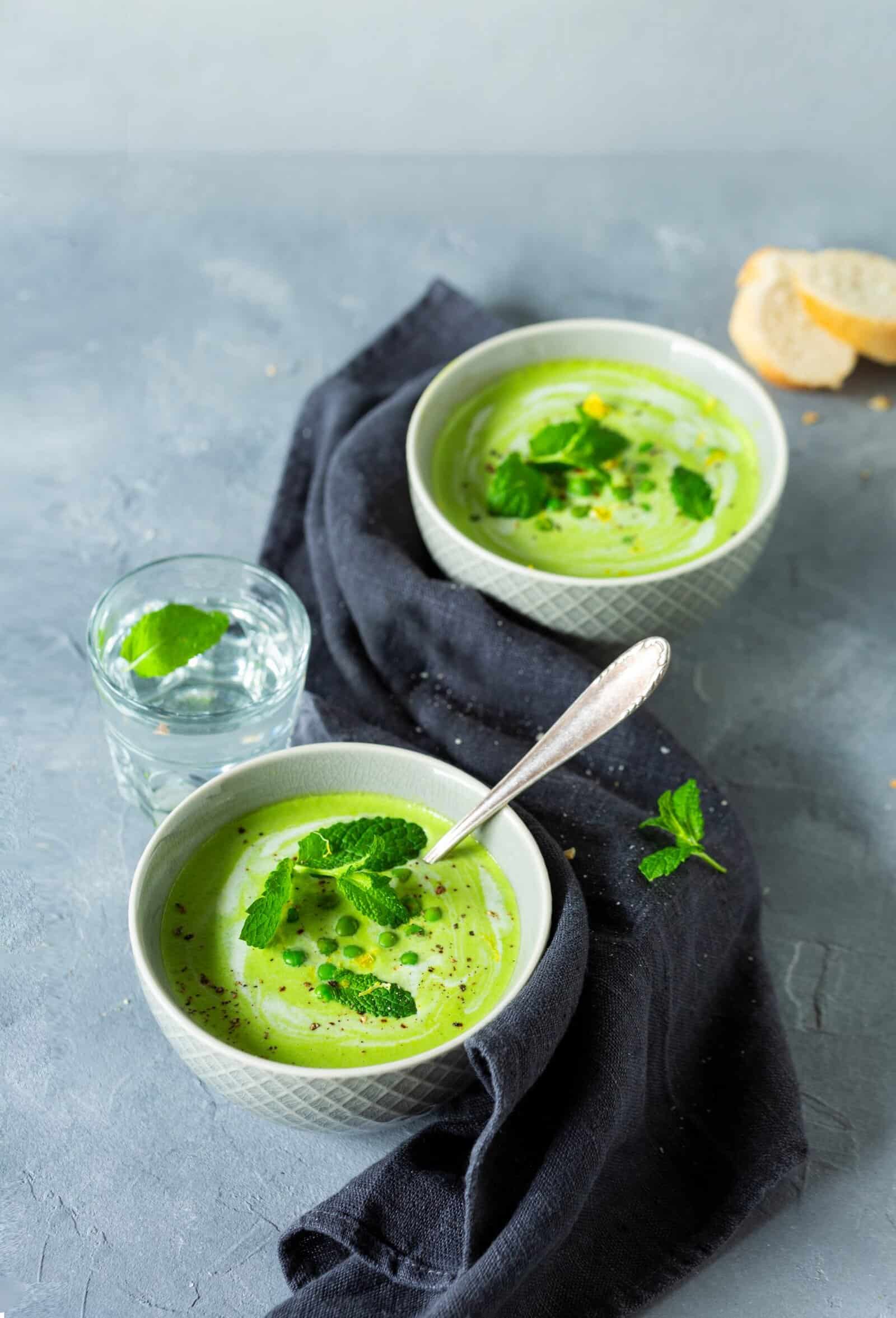 Zwei Schalen mit Erbsensuppe auf grauem Untergrund, mit Minzblättern garniert – Foto: Kathrin Knoll