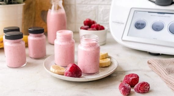 Vier kleine Flaschen mit rotem Joghurt-Getränk, daneben gefrorene Früchte, im Hintergrund ein Thermomix®
