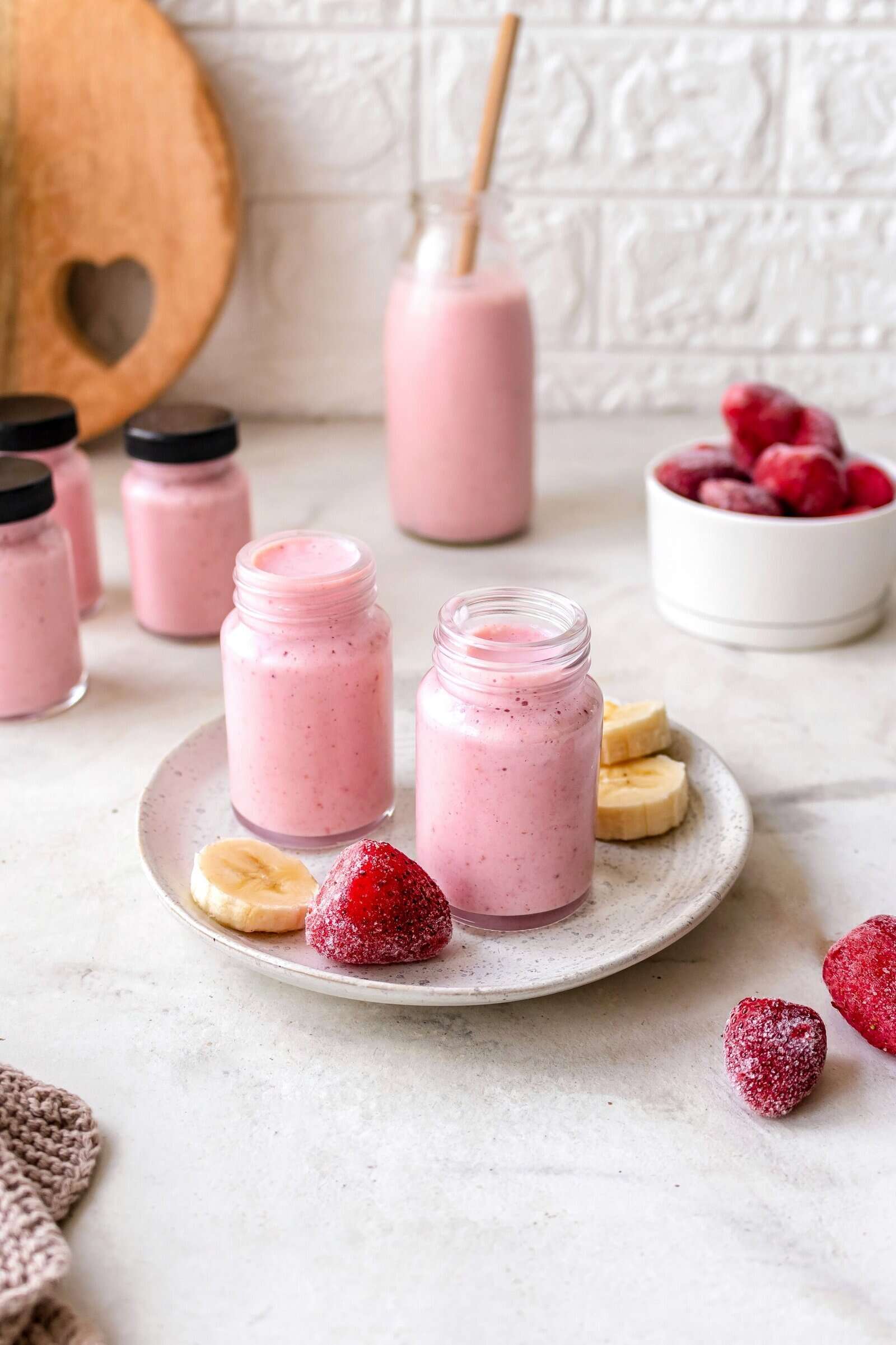 Vier kleine Flaschen mit rotem Joghurt-Getränk, daneben gefrorene Früchte,