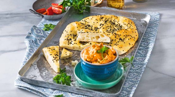 Fladenbrot auf einem grauen Tablett, im Vordergrund eine blaue Schale mit rotem Dip