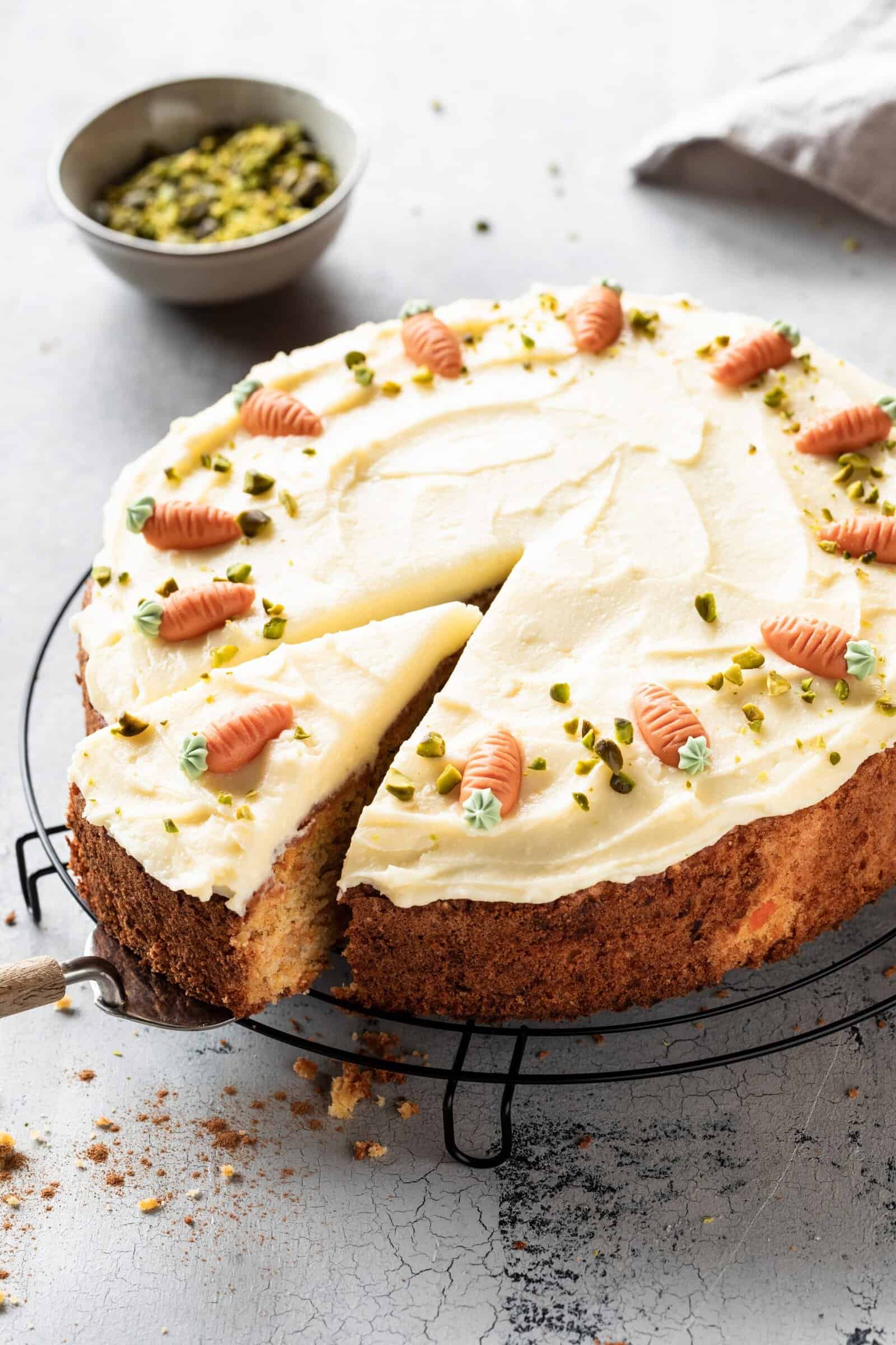 Karottenkuchen mit weißem Frosting und Marzipan-Karotten verziert auf einem Rost, angeschnitten