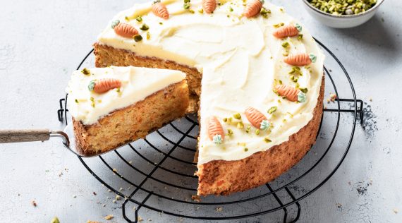 Karottenkuchen mit weißem Frosting und Marzipan-Karotten verziert auf einem Rost, angeschnitten
