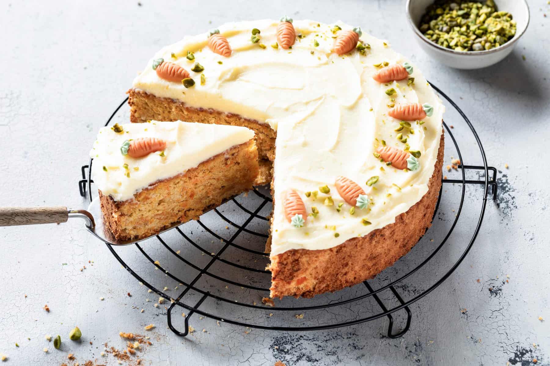 Karottenkuchen mit weißem Frosting und Marzipan-Karotten verziert auf einem Rost, angeschnitten