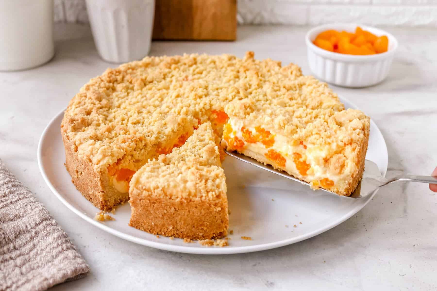 Ein Streuselkuchen mit Cremefüllung, die Mandarinen enthält, angeschnitten auf einem hellen Teller