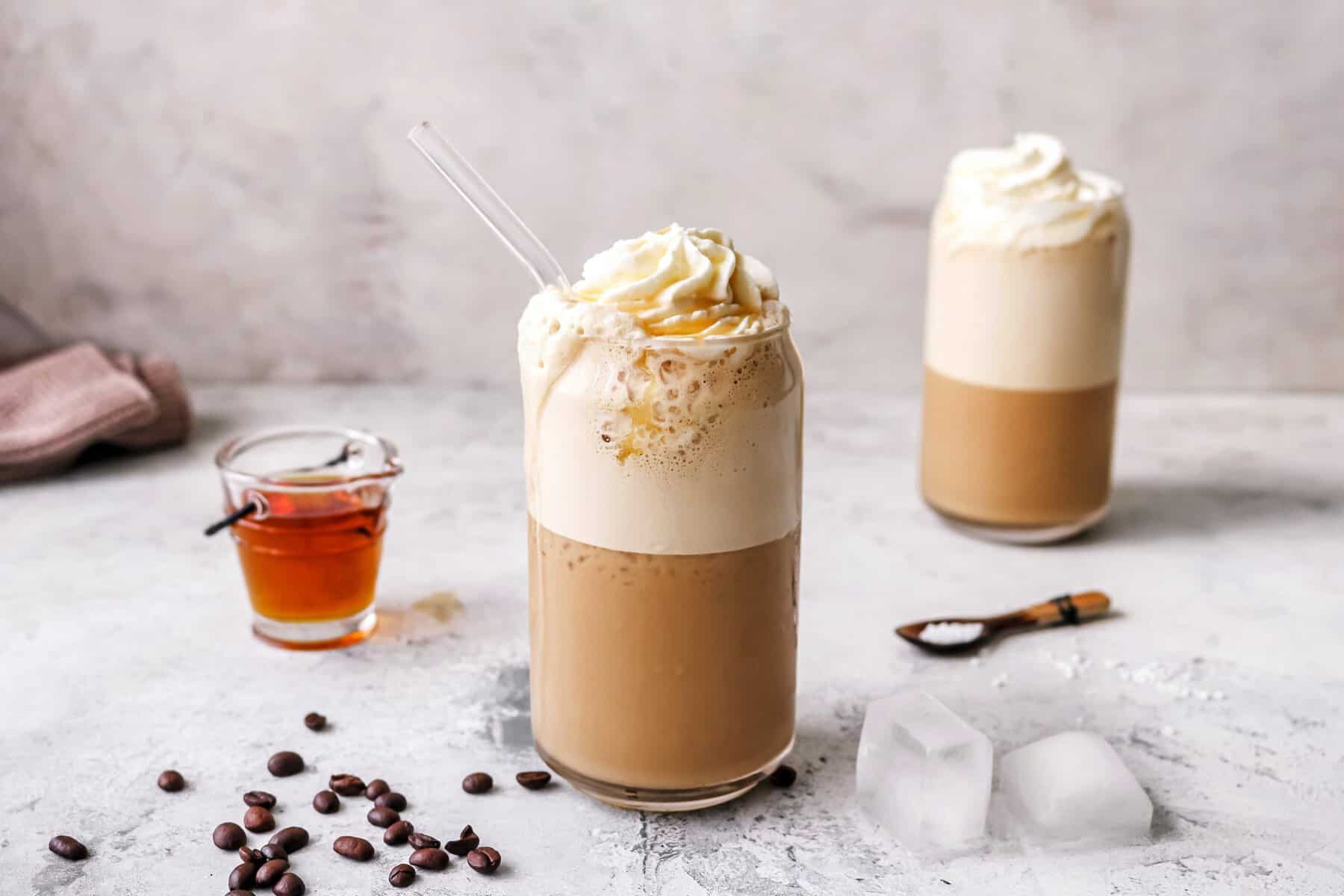https://www.zaubertopf-club.de/rezept/salted-caramel-eiskaffee-thermomix.html zwei Gläser mit einem Kaffeegetränk mit Sahnehaube, daneben Kaffee-Bohnen und Eiswürfel