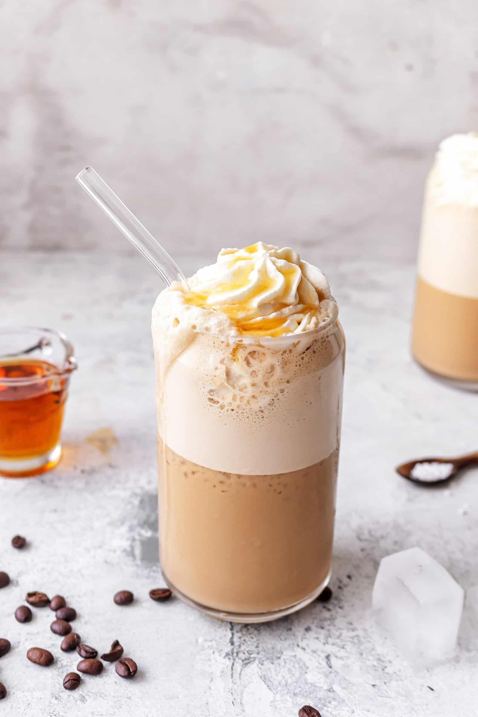 zwei Gläser mit einem Kaffeegetränk mit Sahnehaube, daneben Kaffee-Bohnen und Eiswürfel