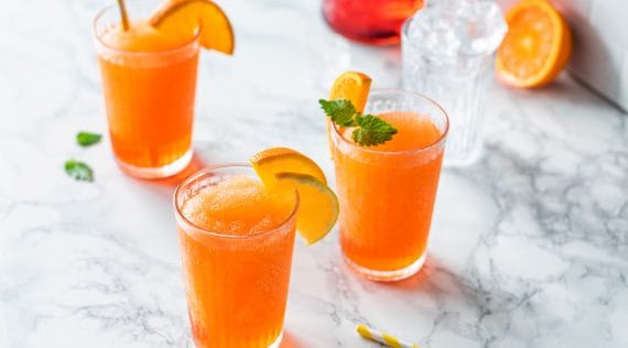 Mehrere Gläser mit einem orangefarbenen Drink, garniert mit Orangenscheiben und Minzblättchen