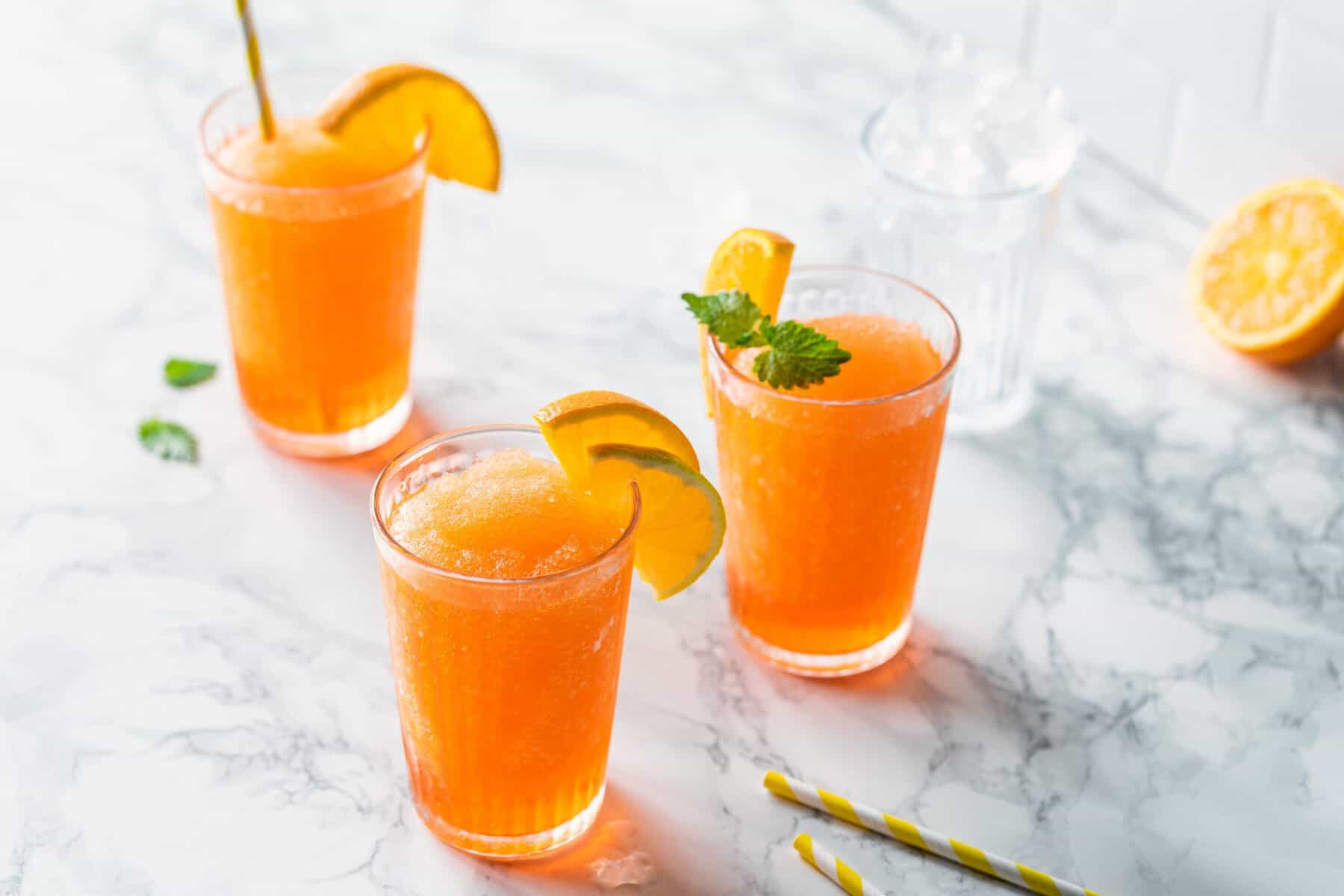 Drei Gläser mit einem orangefarbenen Drink, garniert mit Orangenscheiben