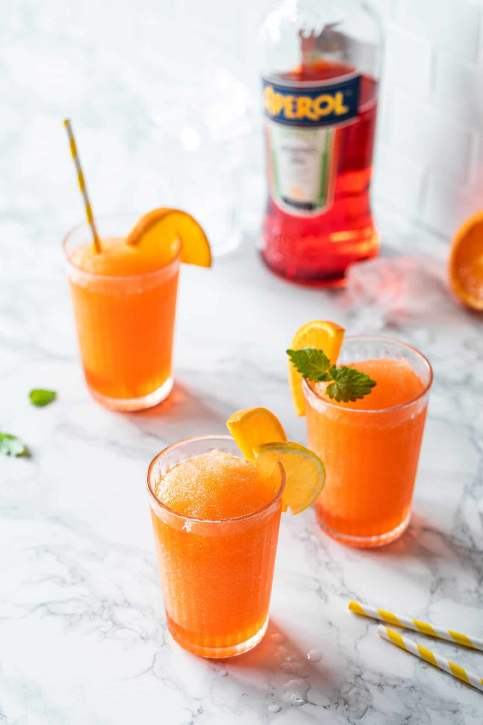 Mehrere Gläser mit einem orangefarbenen Drink, garniert mit Orangenscheiben und Minzblättchen