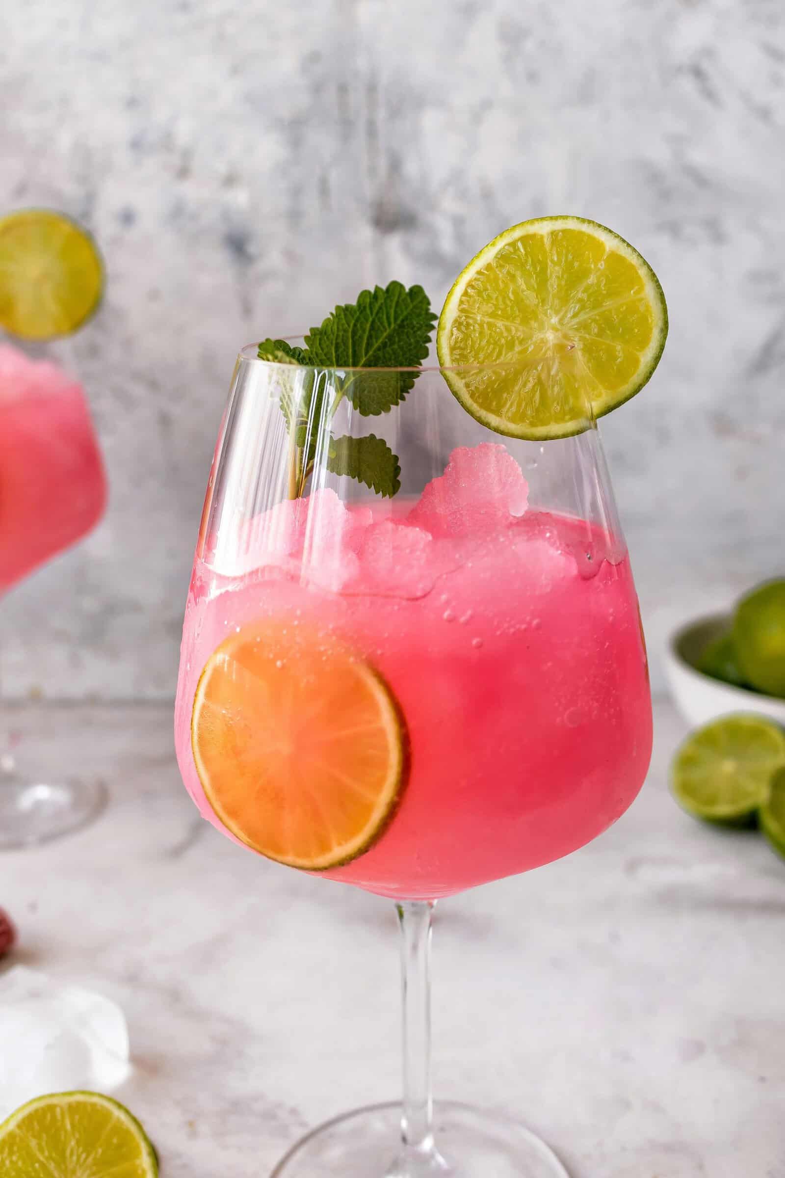 Ein Weinglas mit einem Getränk in pink, mit Eiswürfeln und Limettenscheiben
