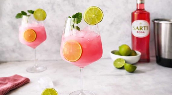 Ein Weinglas mit einem Getränk in pink, mit Eiswürfeln und Limettenscheiben
