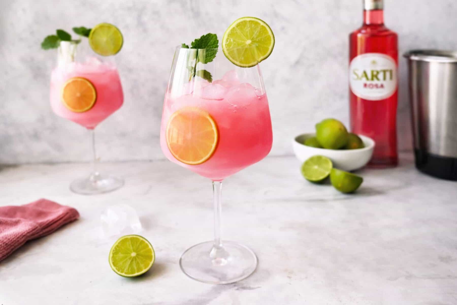 Ein Weinglas mit einem Getränk in pink, mit Eiswürfeln und Limettenscheiben