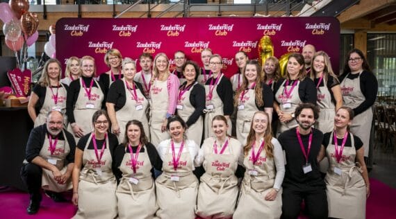 Gruppenfoto mit ca. 20 Menschen vor einer pinkfarbenen Wand, alle tragen Schürzen mit dem Aufdruck 10 Jahre ZauberTopf Club