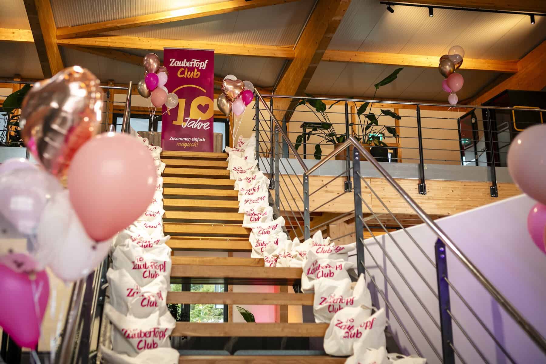 Eine Treppe mit Luftballons dekoriert, auf der Treppe liegen Taschen mit der aufschrift ZauberTopf Club